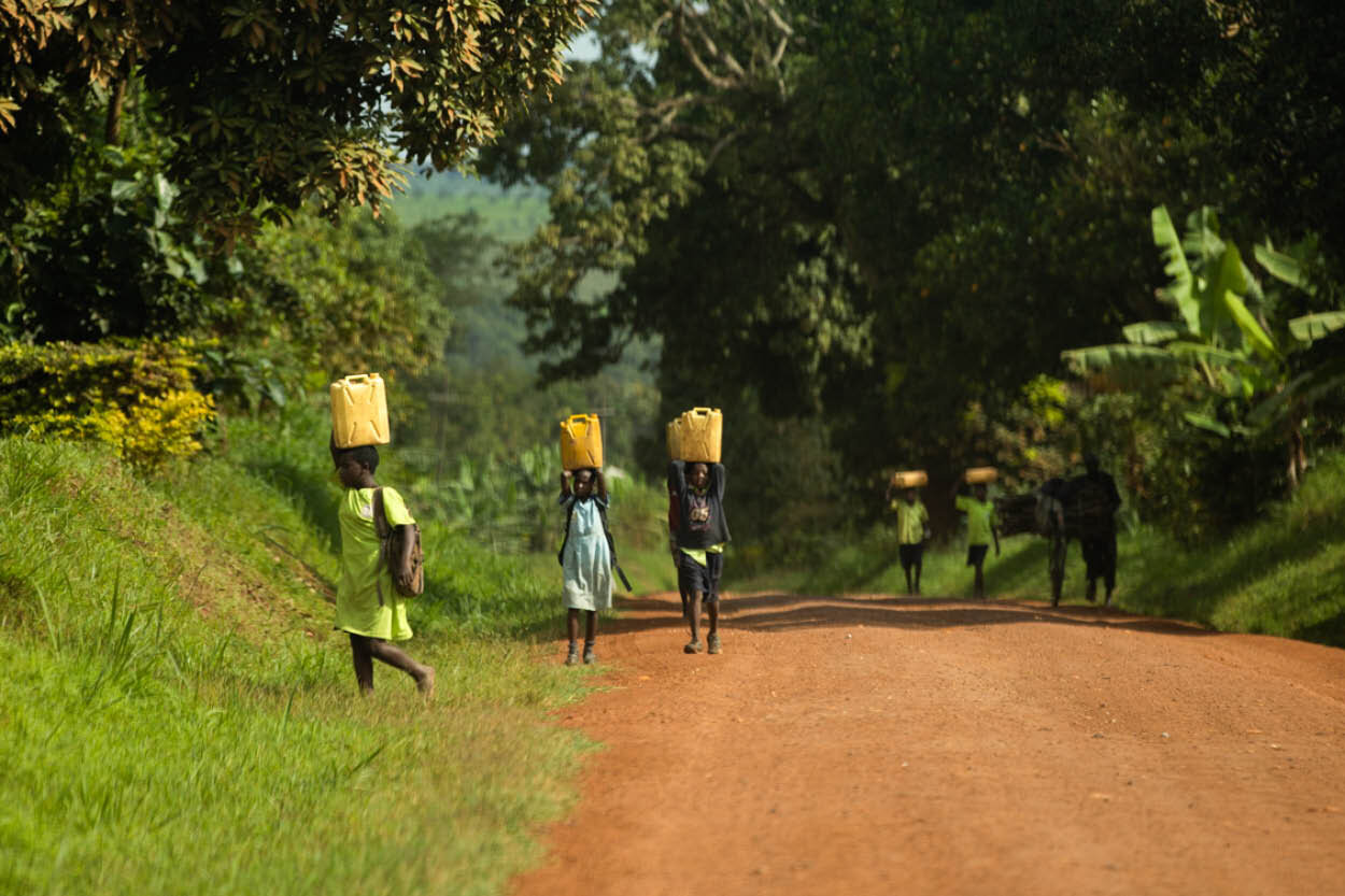 children wearing backpacks carry jerrycans filled with water on their heads