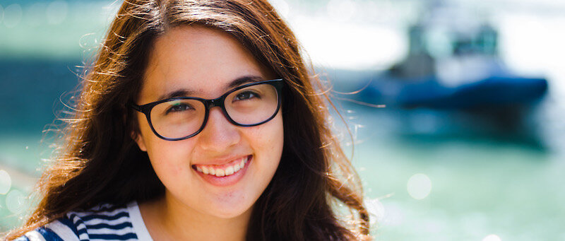 girl with glasses smiling in front of a blue background
