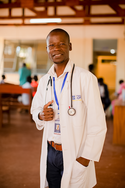 doctor in a medical coat stands smiling at the camra