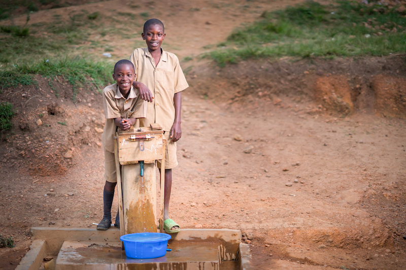 school children standing behind a water well project in africa