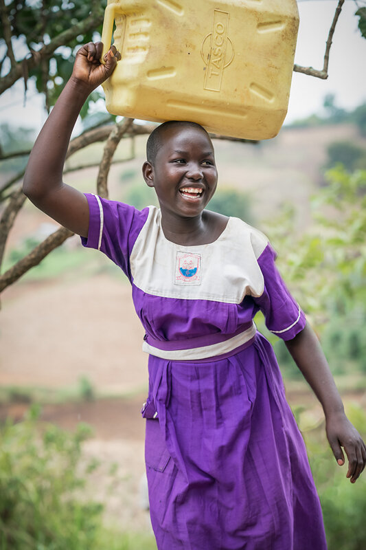 girl wearing school uniform carrying her jerrycan filled with clean water on her head