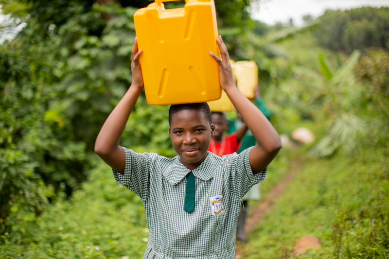 ugandan girl in school uniform carries jerrycan on her head