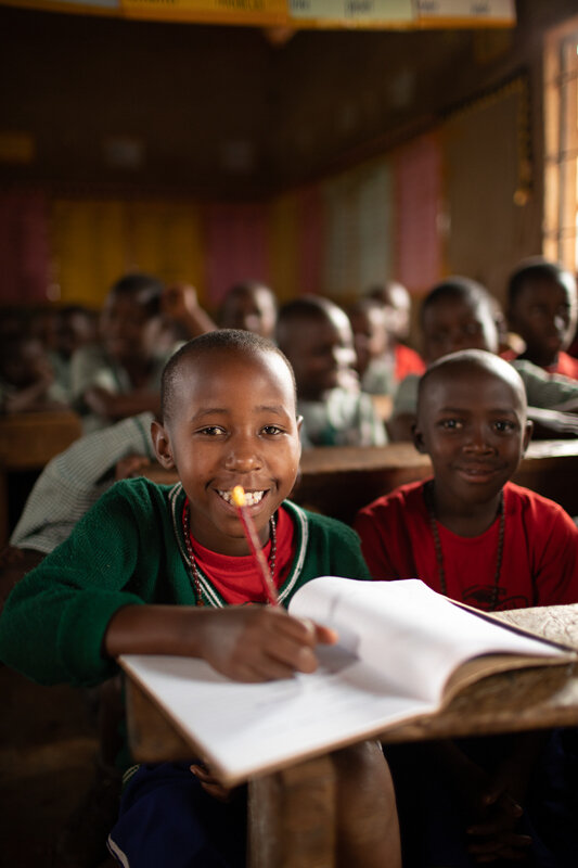 boy in school, holding pencil and smiling as he writes