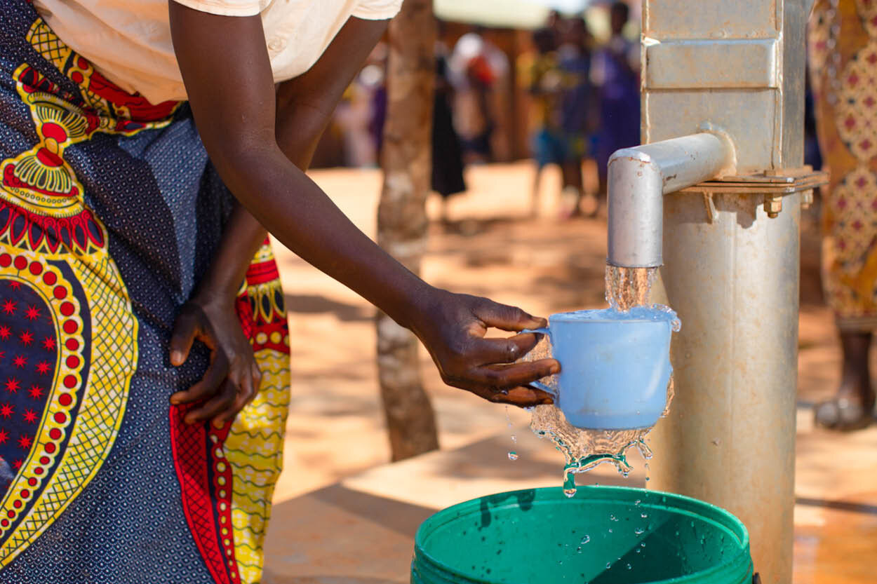 woman draws water from a well into her cup